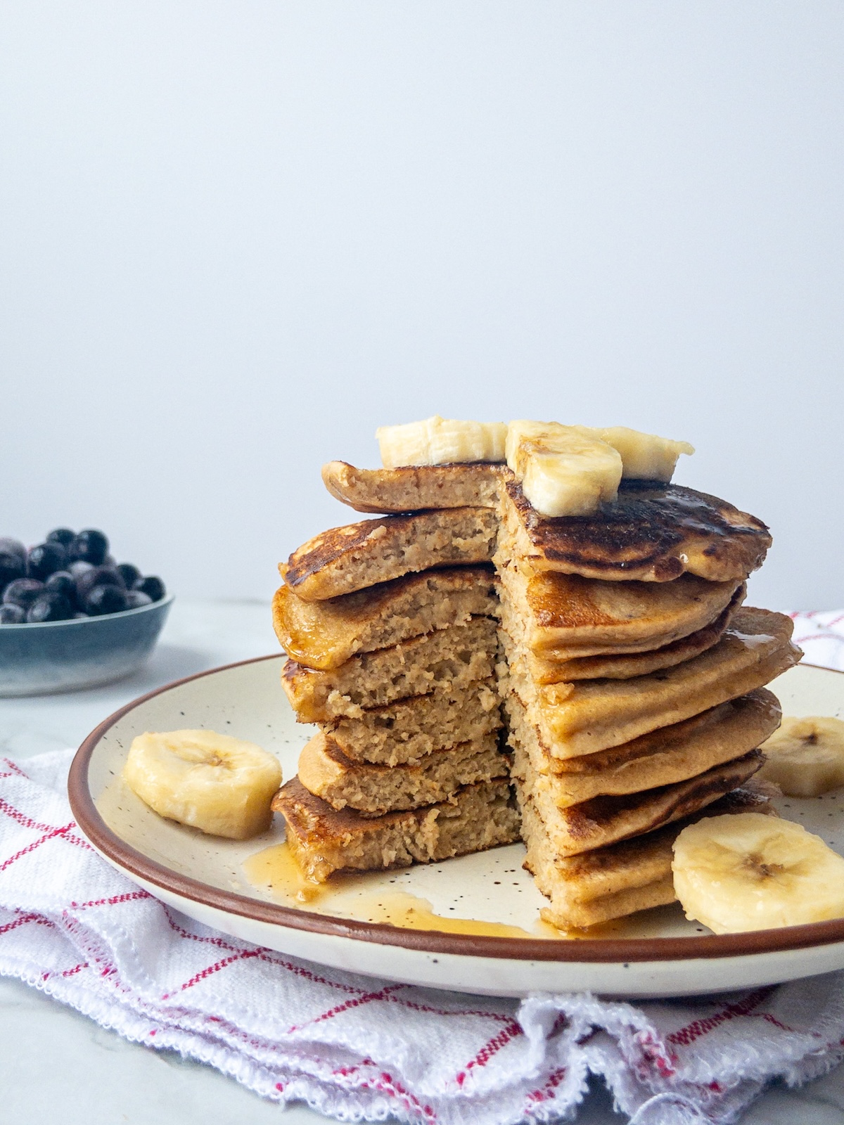 A stack of banana pancakes with maple syrup drizzled on top. A big piece has been cut out