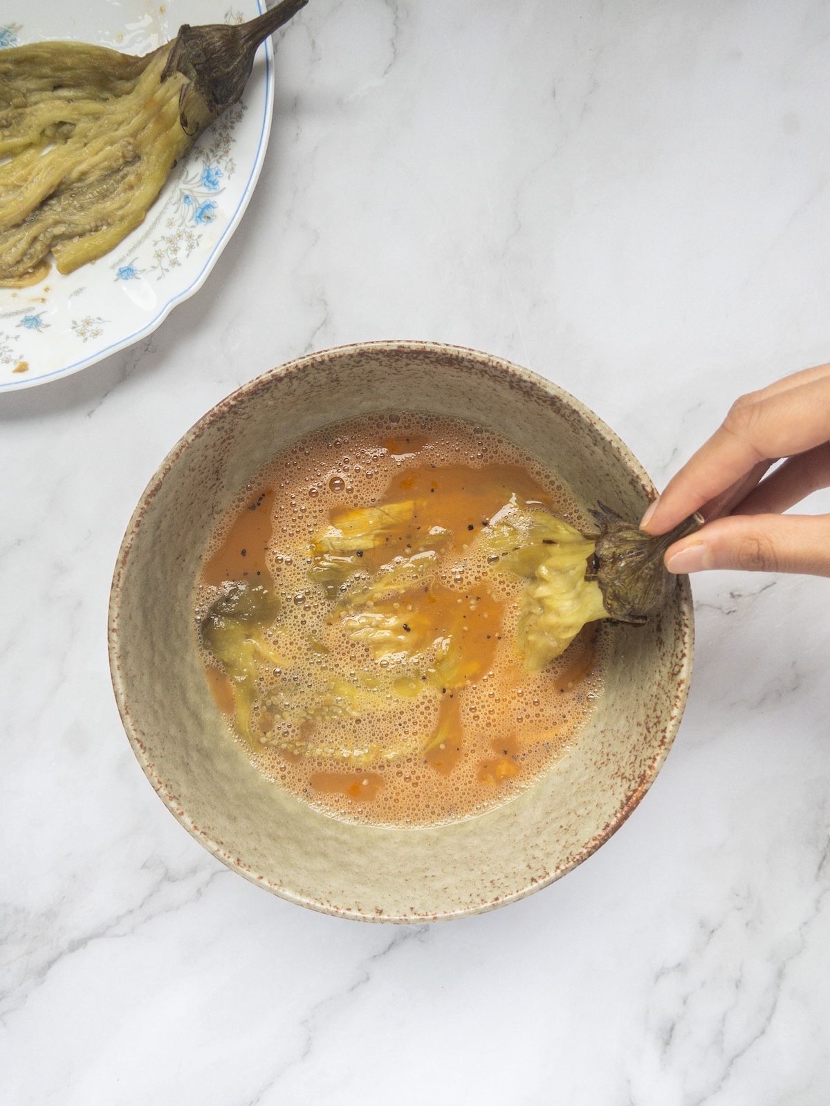 a roasted eggplant being dipped into an egg mixture in a bowl