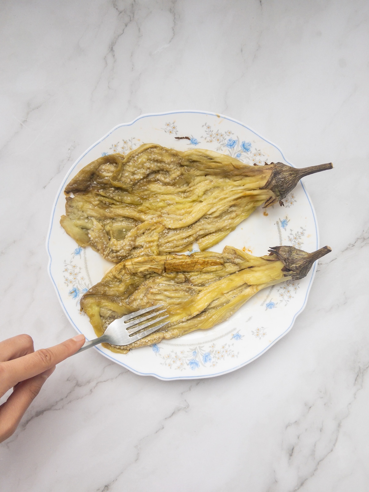 roasted eggplants being mashed by a fork on a plate