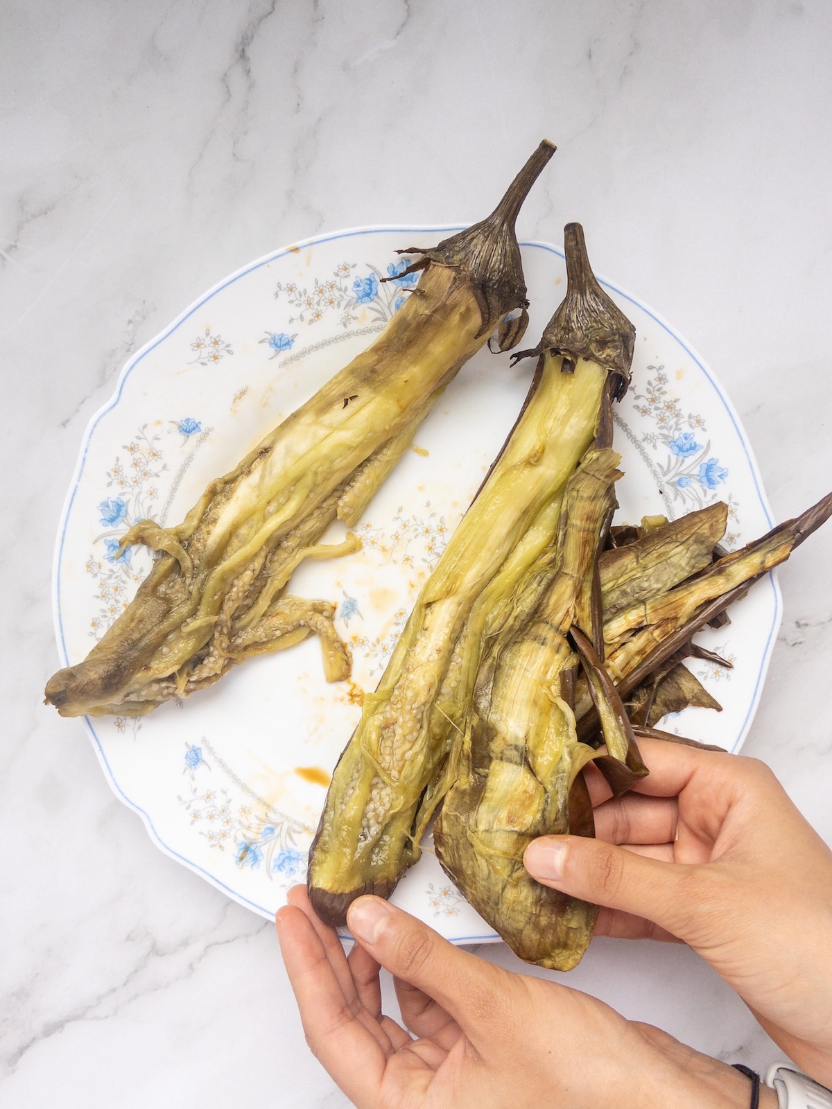 a person peeling the skin of a roasted eggplant by hand