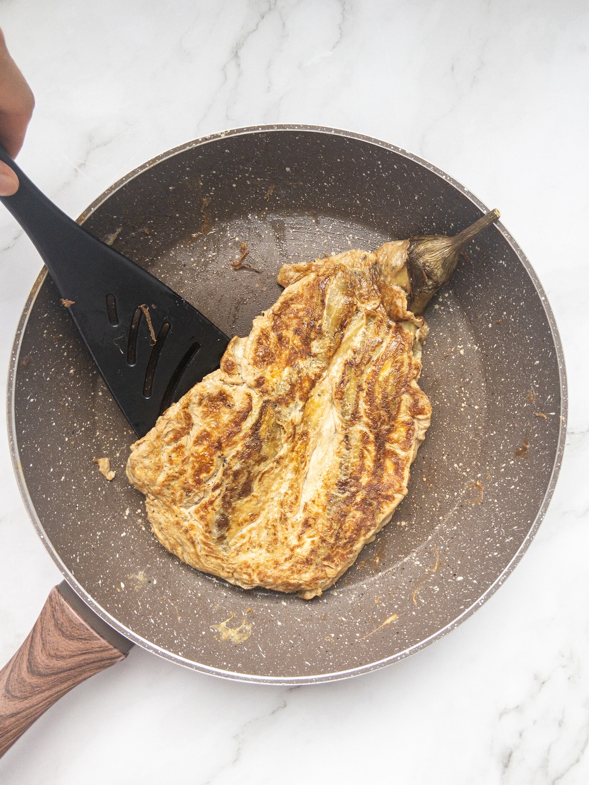 a roasted eggplant covered in eggs being fried in a pan