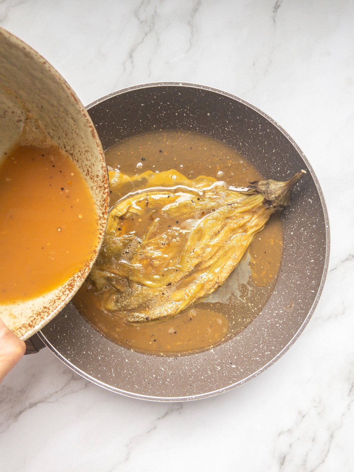 a roasted eggplant covered in eggs being fried in a pan