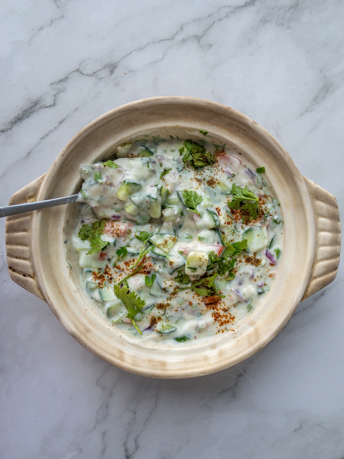 A spoon stirring a mixed vegetable raita served in a bowl