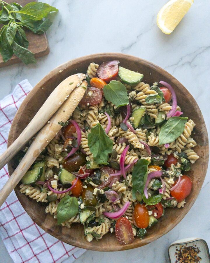 Pesto pasta salad in a wooden bowl topped with fresh basil
