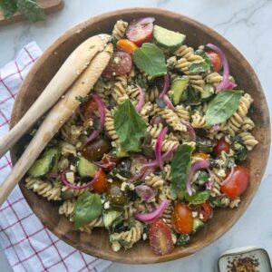 Pesto pasta salad in a wooden bowl topped with fresh basil