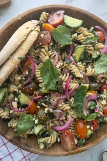 Pesto pasta salad in a wooden bowl topped with fresh basil
