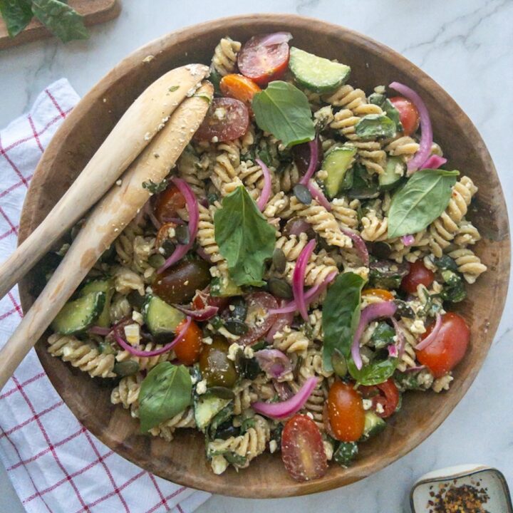 Pesto pasta salad in a wooden bowl topped with fresh basil