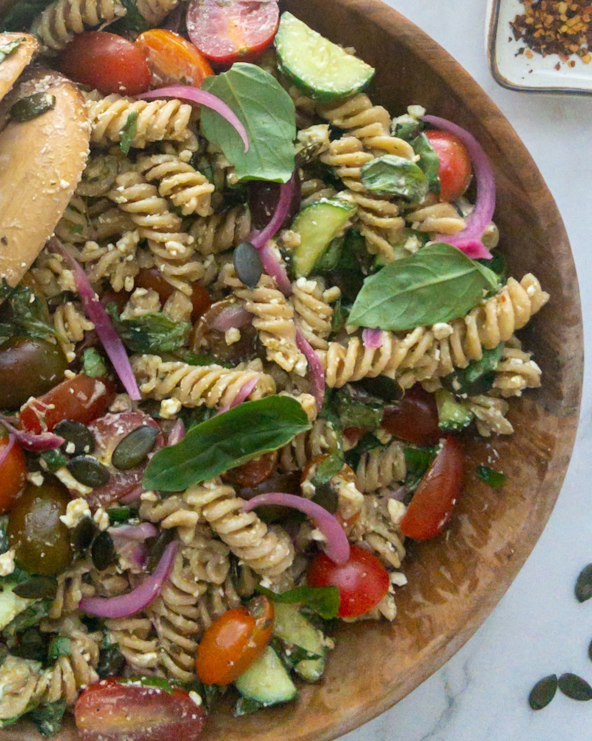 a close up of Pesto pasta salad in a wooden bowl topped with fresh basil