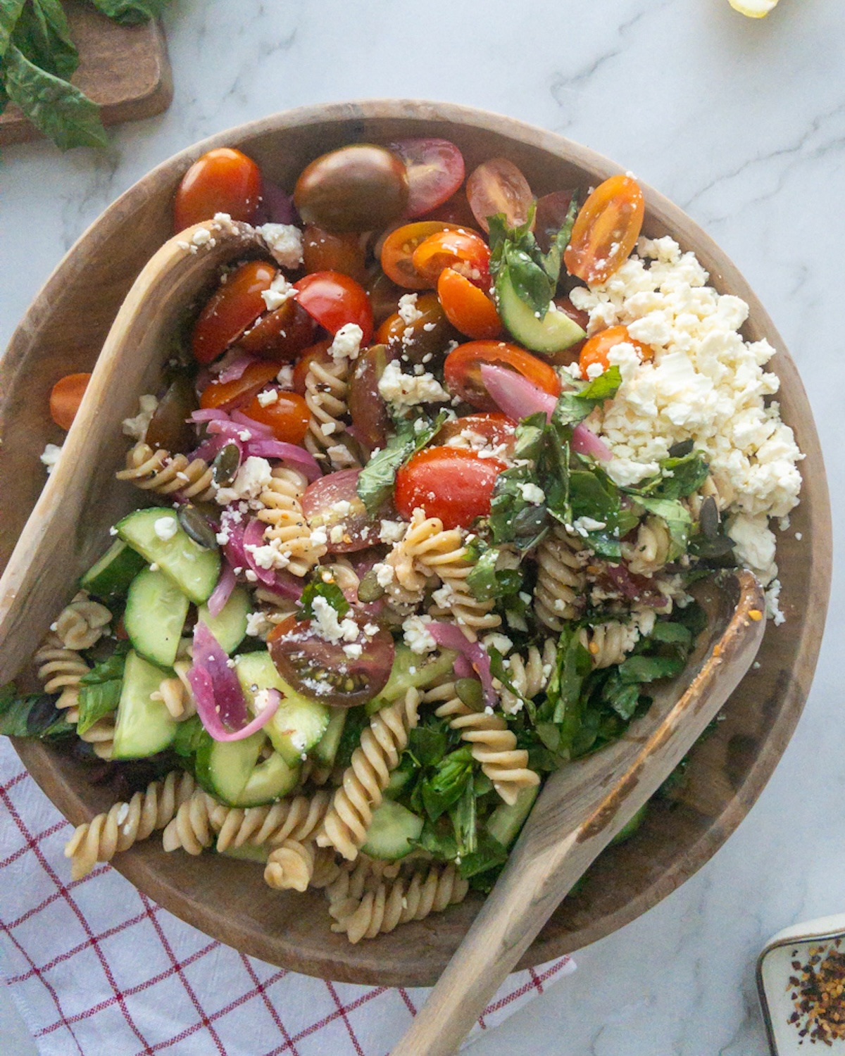Pesto pasta salad in a wooden bowl being mixed together