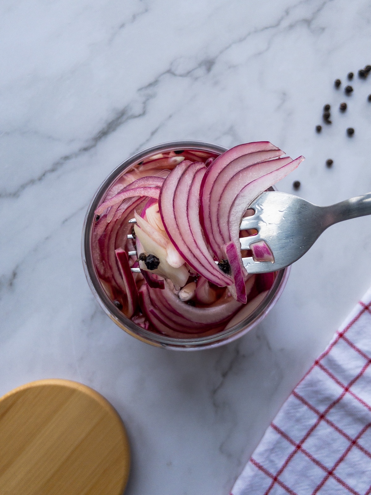 Pickled red onions on a fork on top of a glass jar