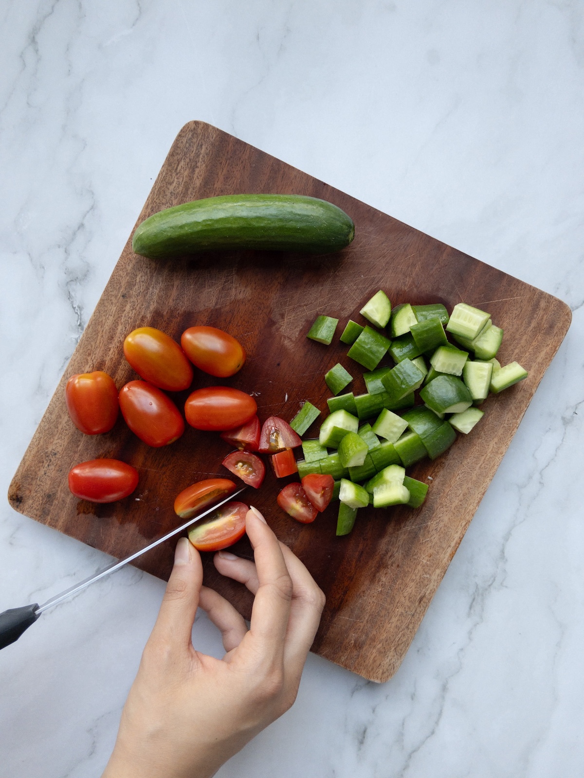 tomatoes and cucumbers being chopped on a wooden chopping board