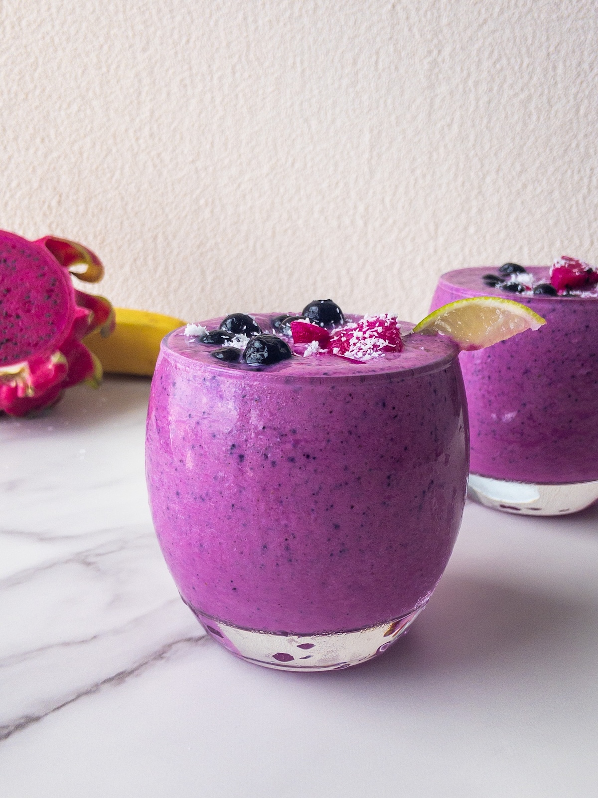 a bright pink smoothie presented in a glass topped with fresh fruit