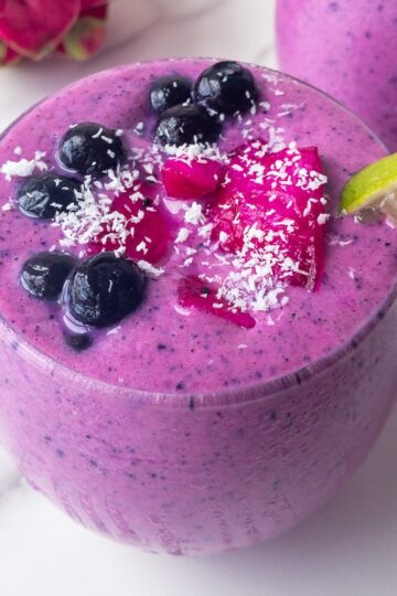 a bright pink smoothie presented in a glass topped with fresh fruit