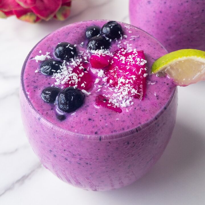 a bright pink smoothie presented in a glass topped with fresh fruit