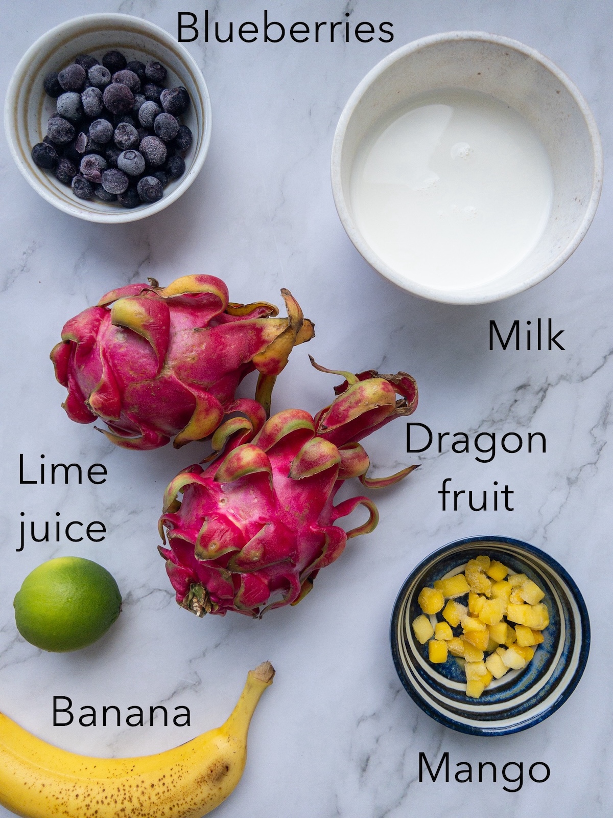 ingredients for a smoothie on a table including dragon fruit, banana and blueberries.