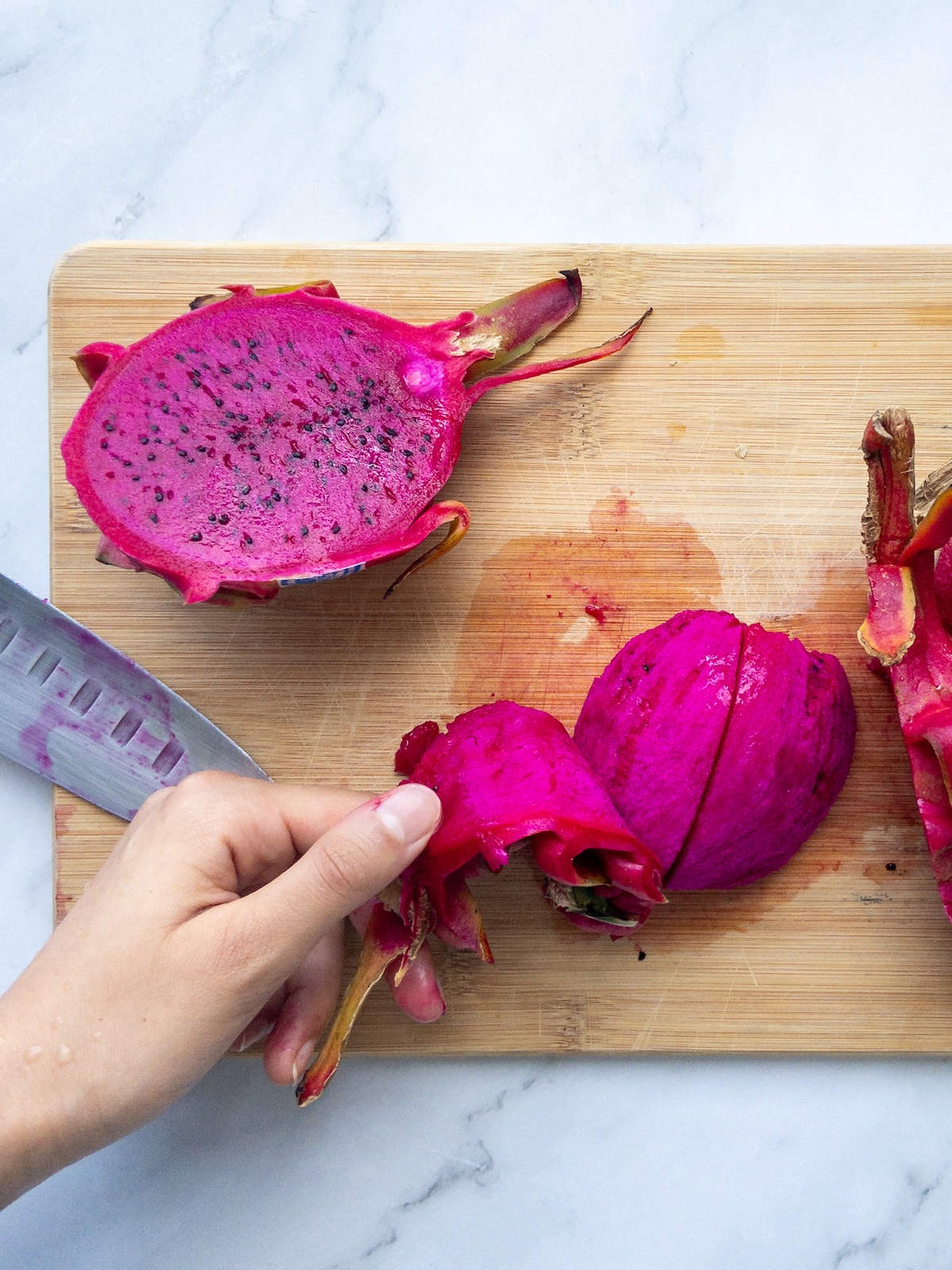dragon fruit skin being peeled off on a wooden cutting board