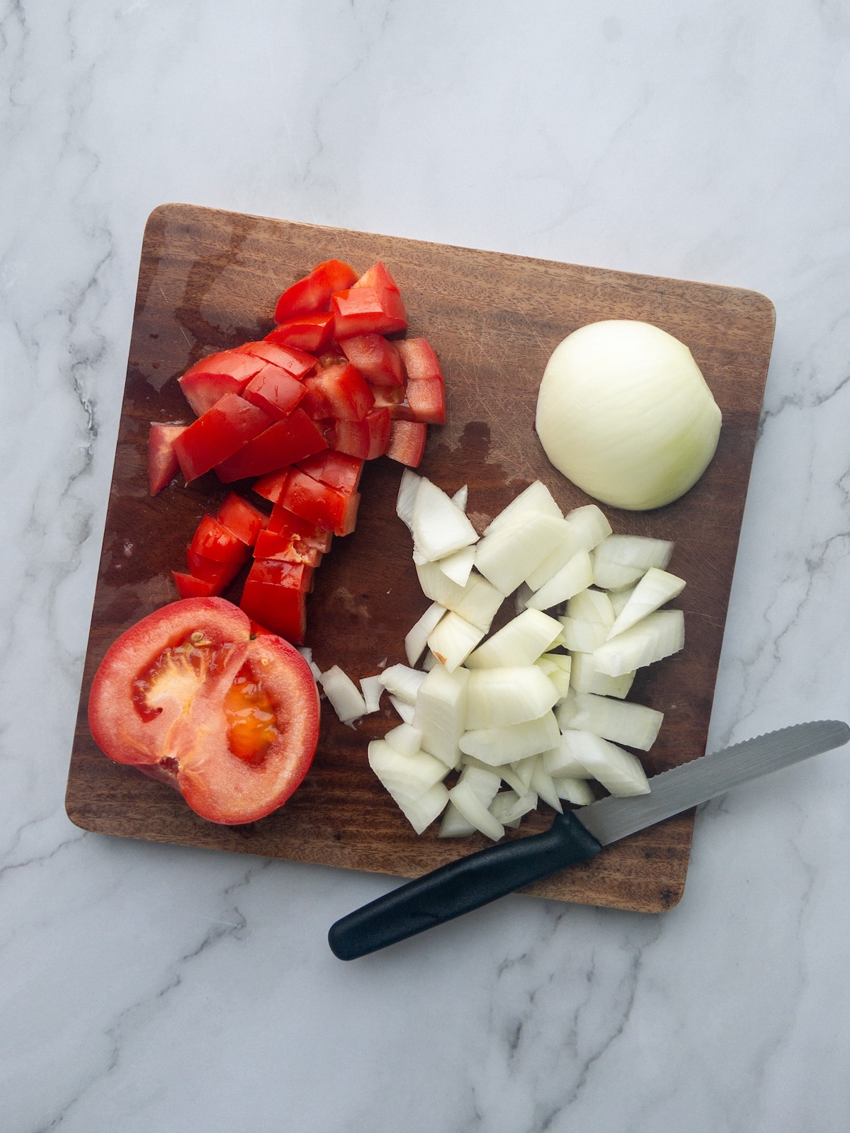 A tomato and onion being chopped in a wooden board