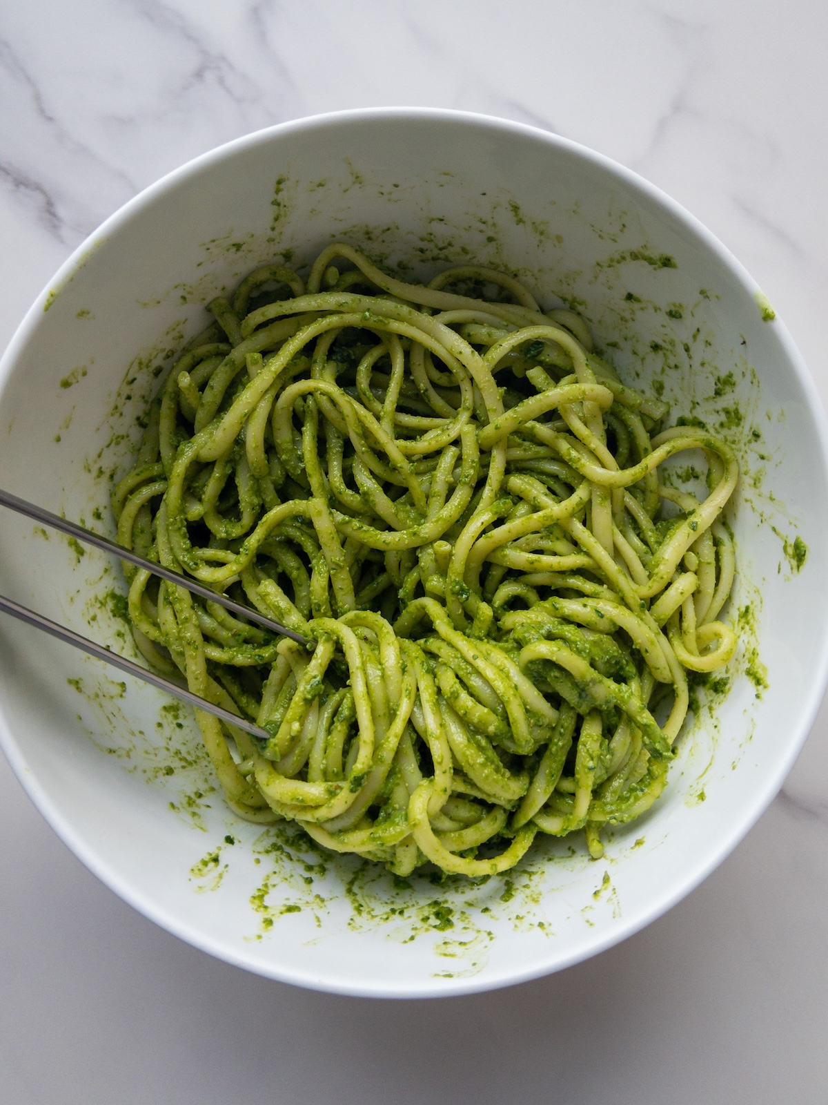boiled linguine mixed with homemade basil pesto in a large bowl