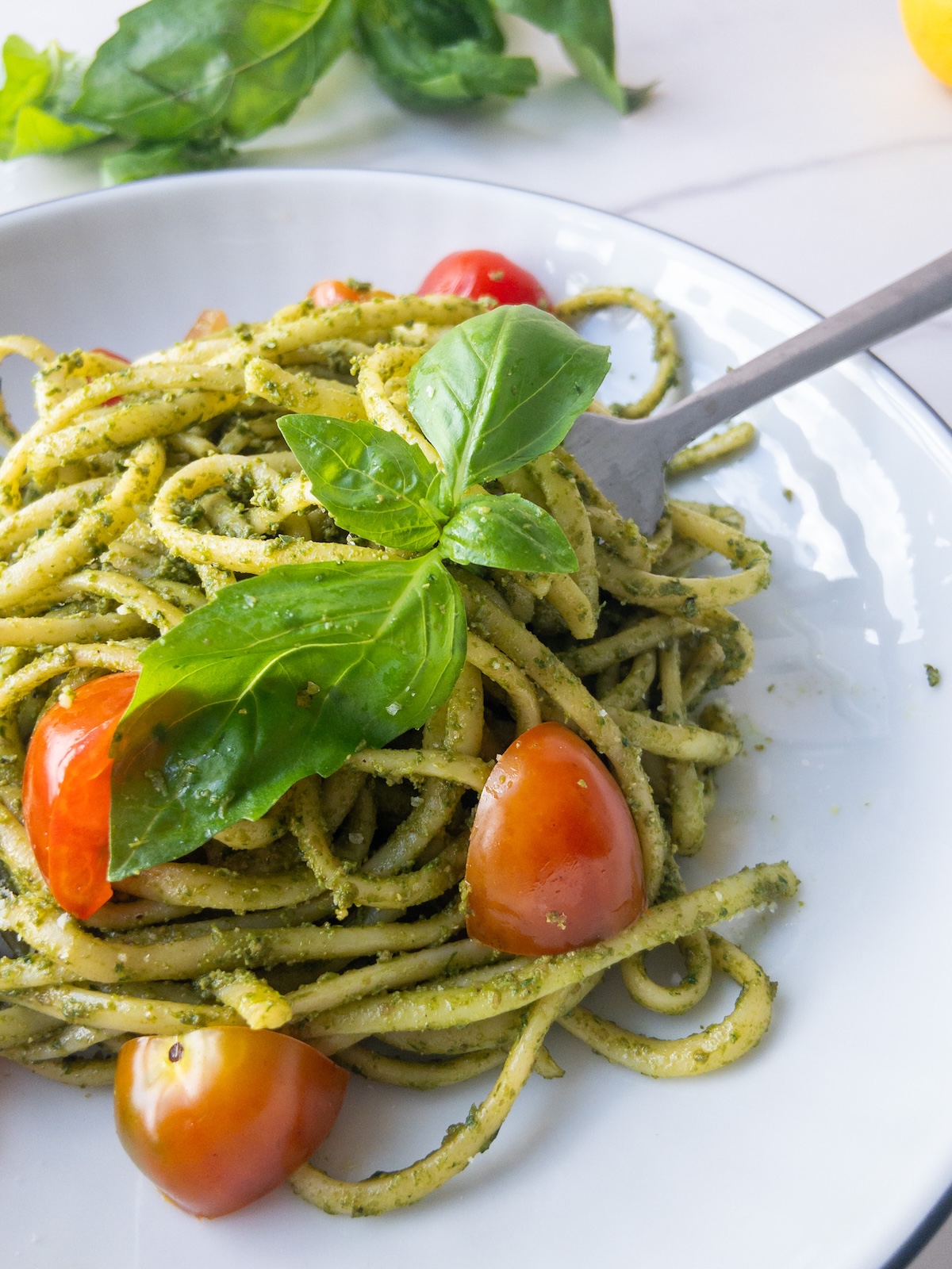 pasta with pesto served in a plate topped with fresh basil and cherry tomatoes