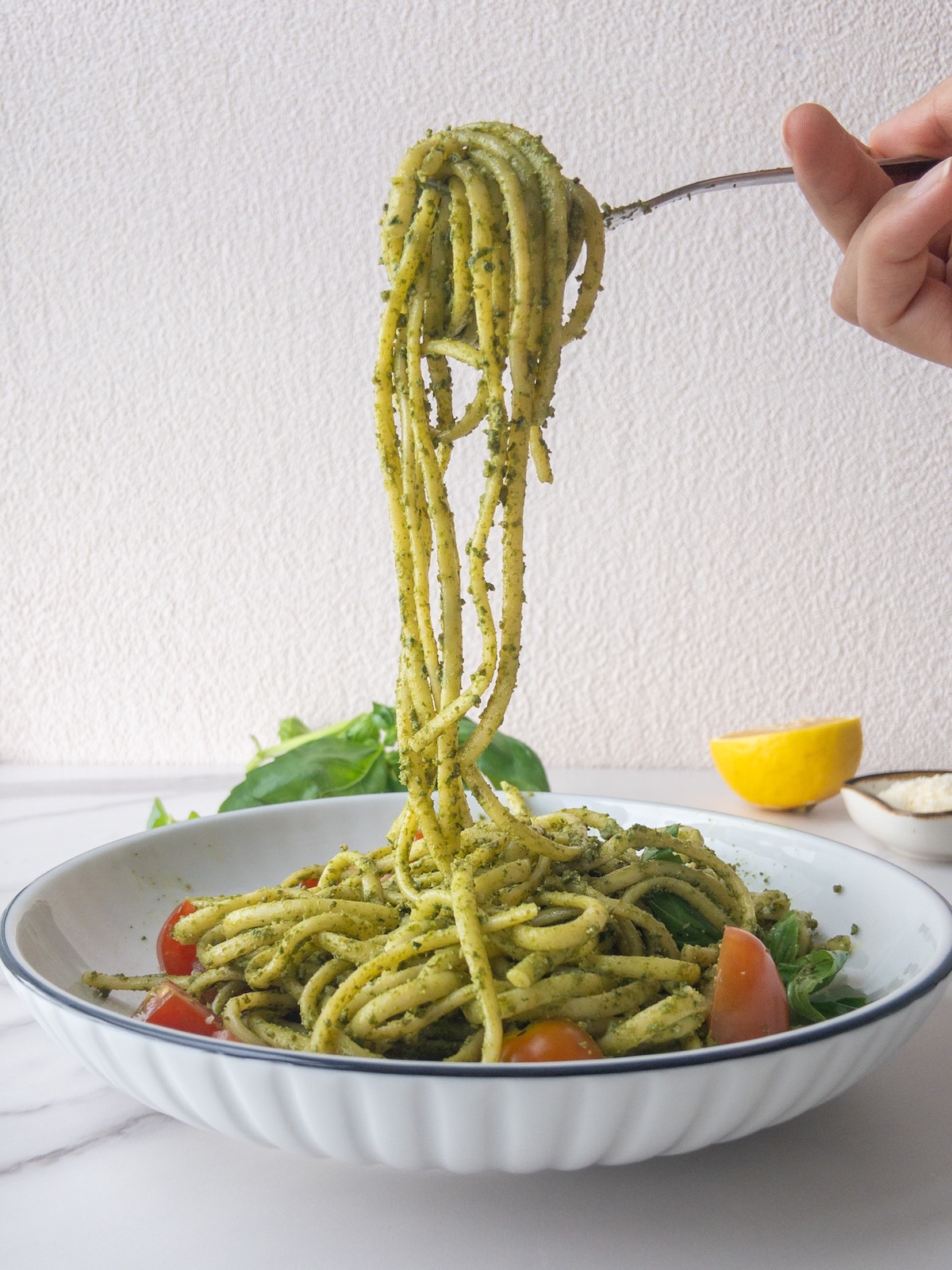 pasta with pesto served in a plate topped with fresh basil. A fork is holding up some pasta