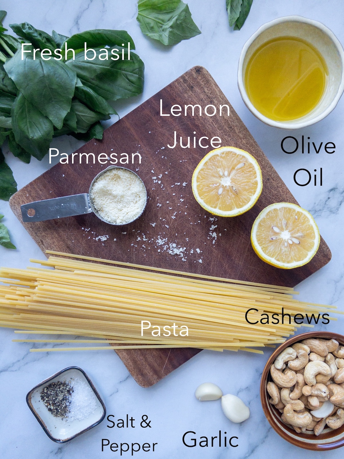 ingredients laid out on a table and wooden board for a homemade pesto pasta recipe.