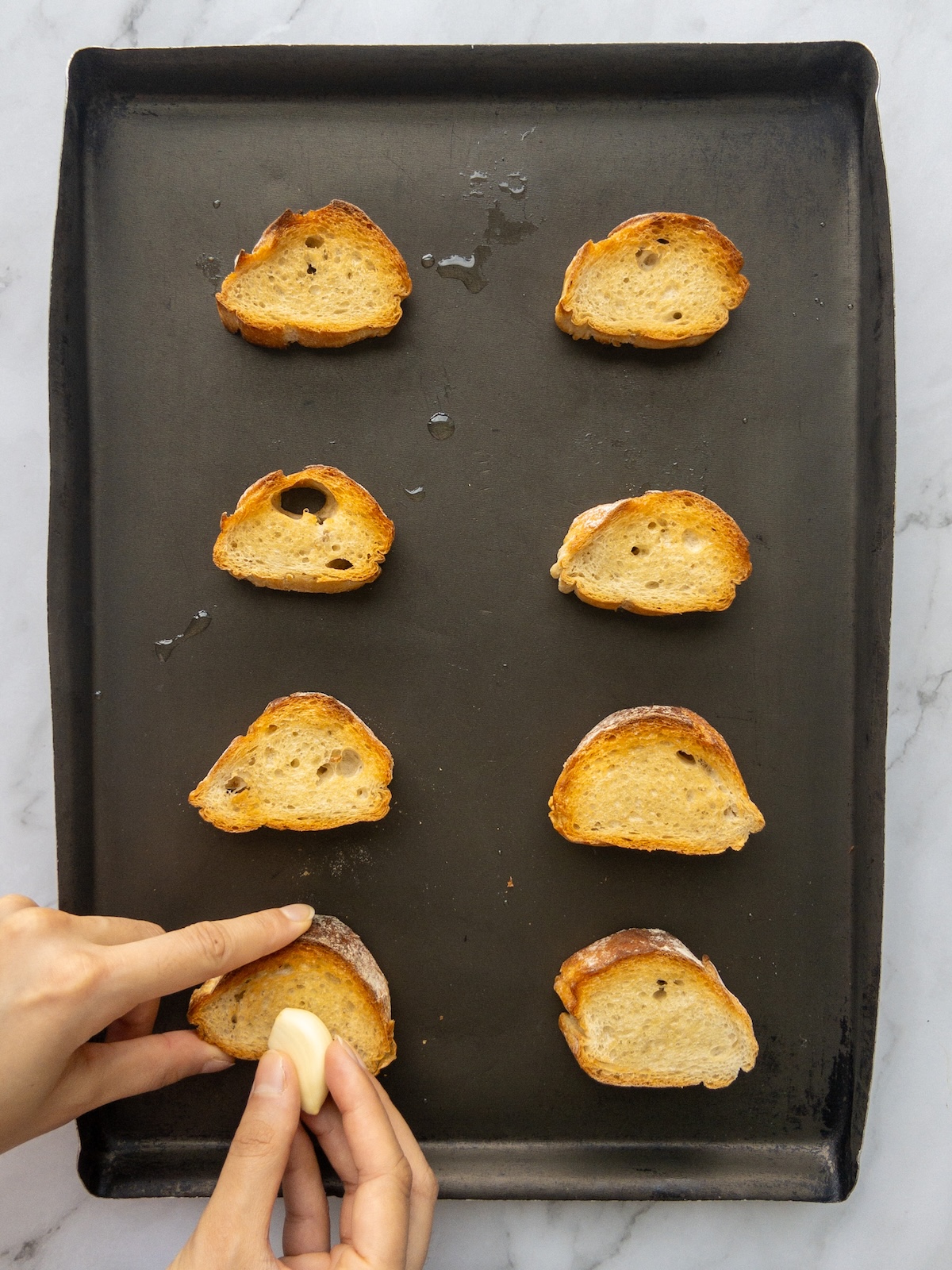 Toasted slices of baguette being rubbed with garlic