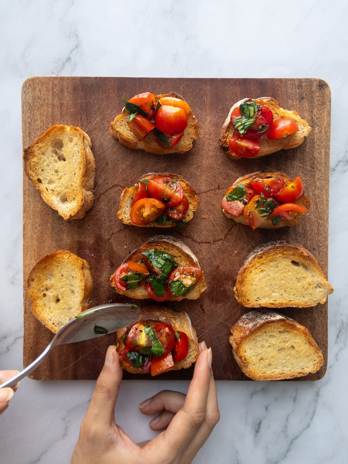 Tomatoes being spooned onto slices of baguette