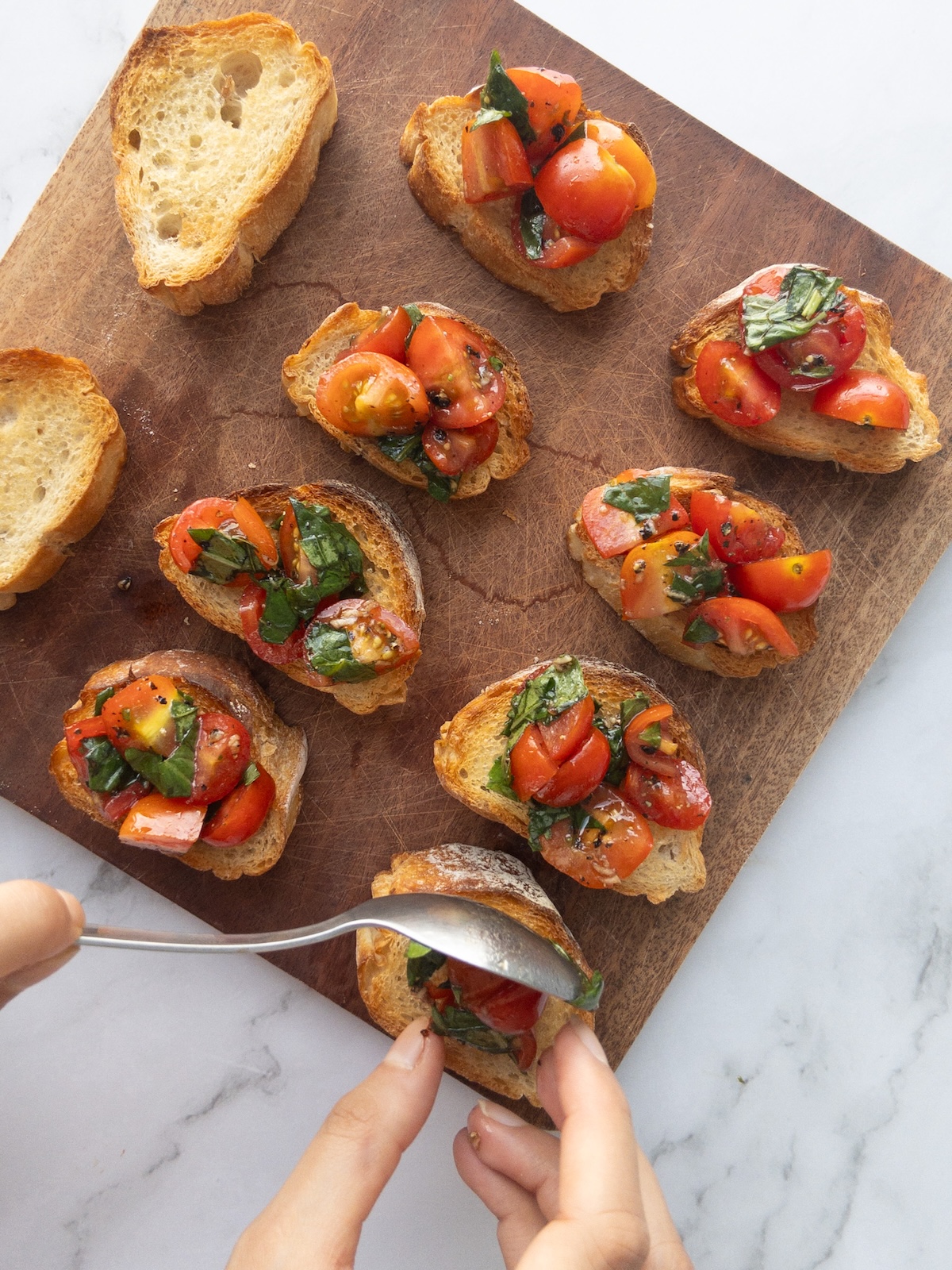 Tomatoes being spooned onto slices of baguette