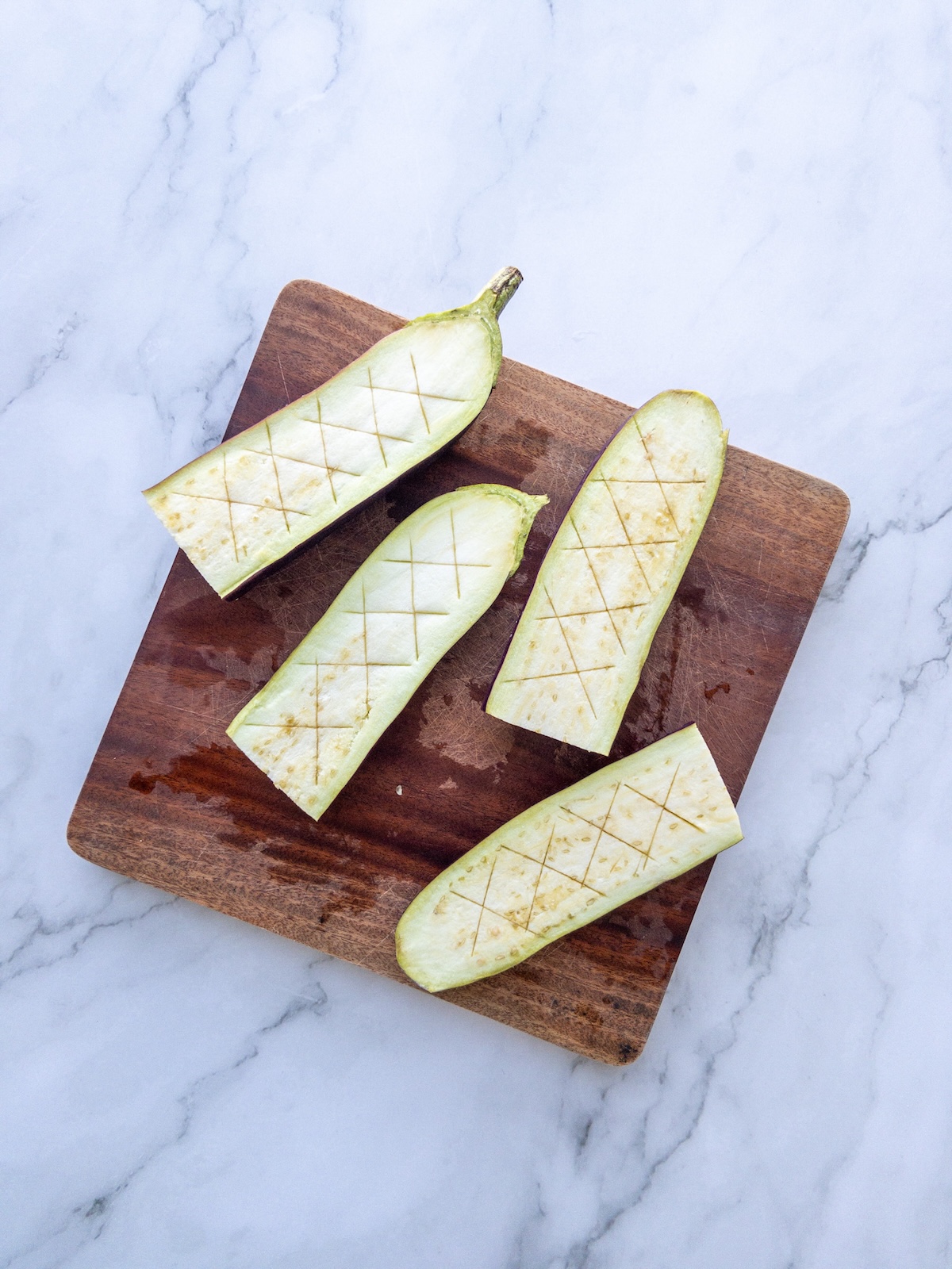 Scored aubergines on a wooden board