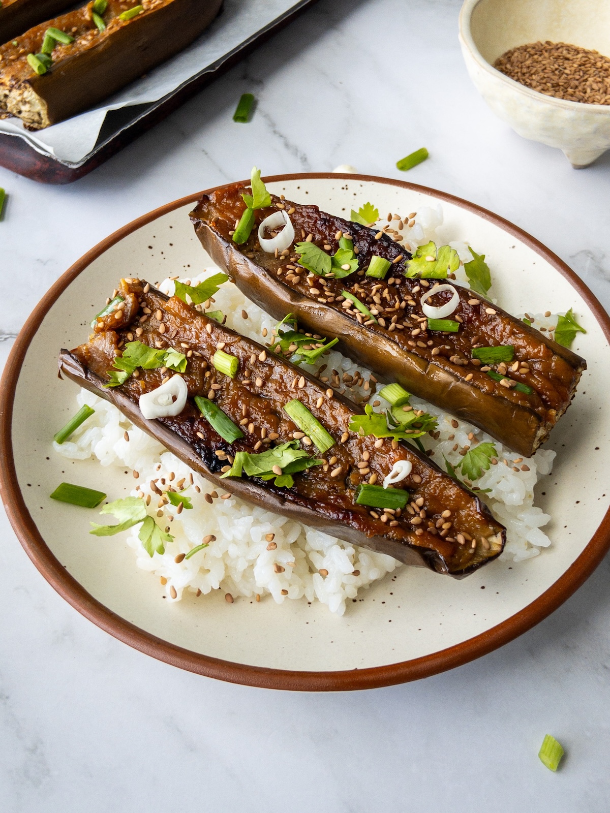 Sticky aubergines served with rice topped with sesame seeds, green onions and cilantro.