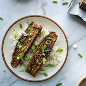 Sticky aubergines served with rice topped with sesame seeds, green onions and cilantro.