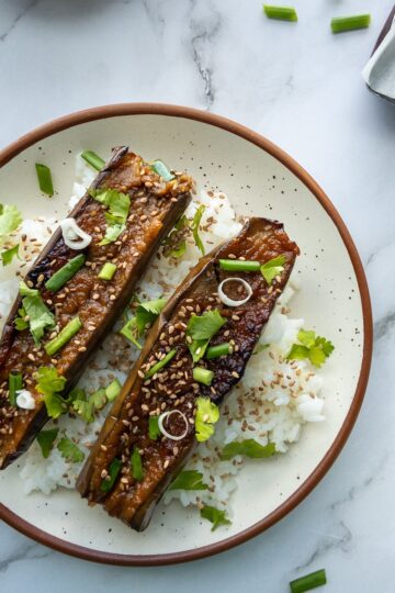 Sticky aubergines served with rice topped with sesame seeds, green onions and cilantro.